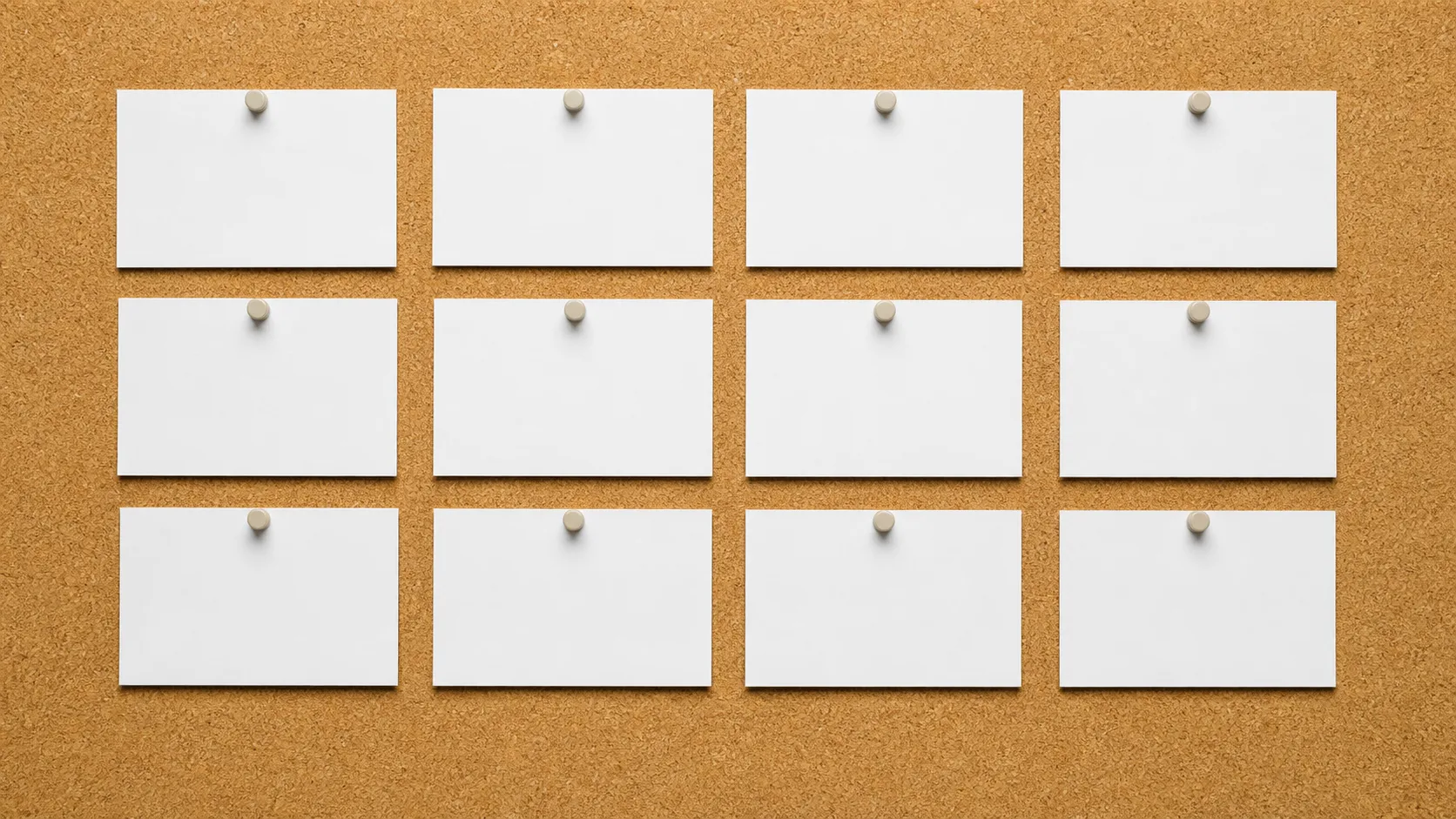 Twelve blank white cards pinned in rows on a cork board