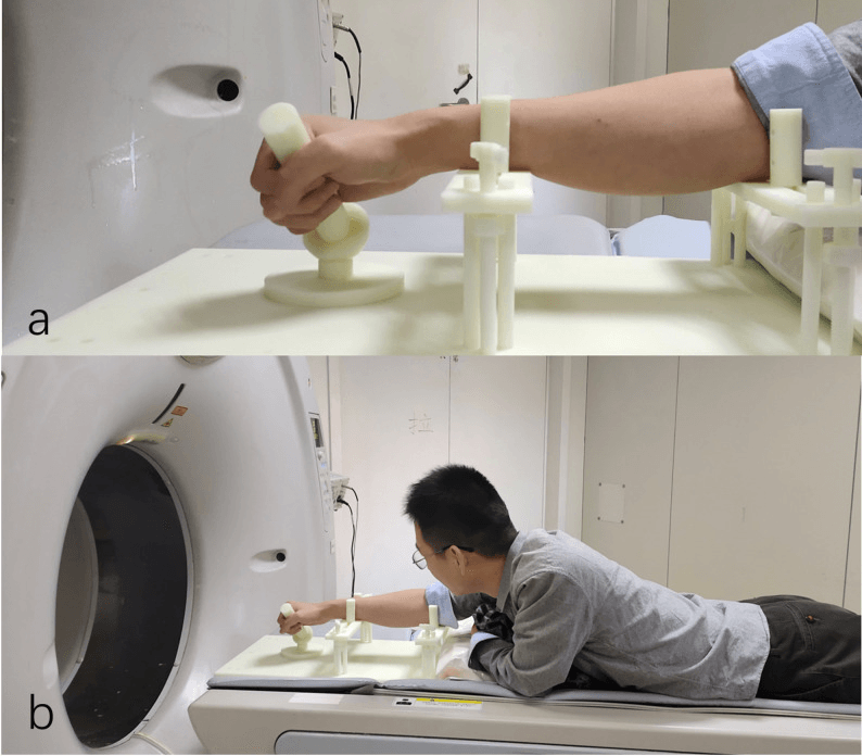 Two panels: (a) a hand gripping the handle of a motion guide with the forearm held in supports; (b) a participant lying prone on the CT table with the arm extended toward the scanner gantry