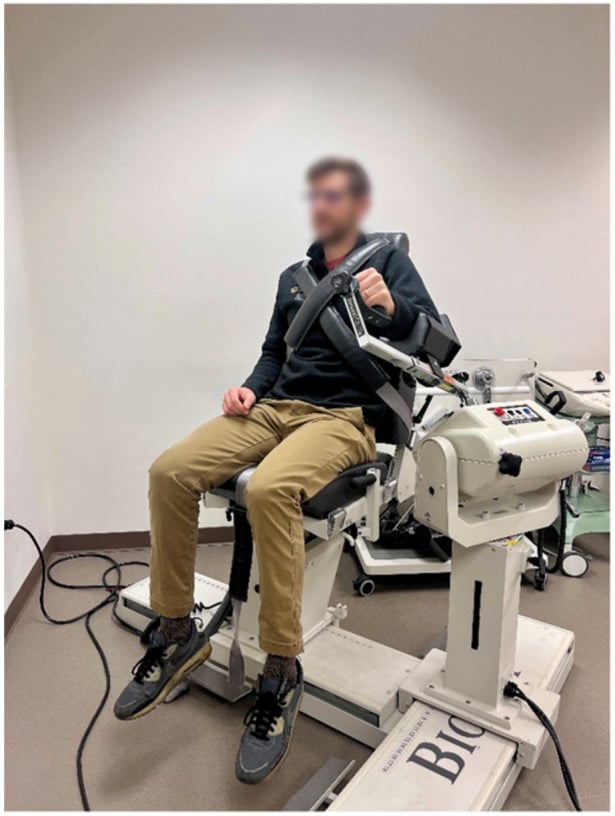 Athlete seated and strapped at the trunk, gripping the handle of an isokinetic dynamometer for shoulder internal and external rotation testing