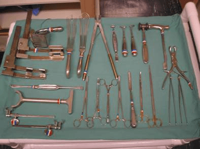 A metal surgical instrument tray laid out on a green drape, showing retractors, osteotomes, a mallet, elevators, forceps and scissors arranged in rows