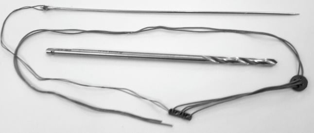 Photograph of a suture-button construct with drill bit, straight needle, oblong endobutton, round button and heavy suture
