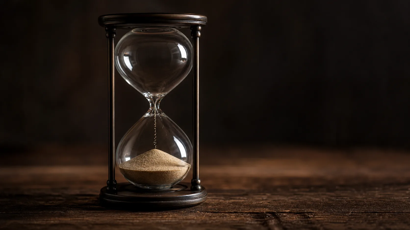 An hourglass with the sand part run through resting on a dark wooden surface