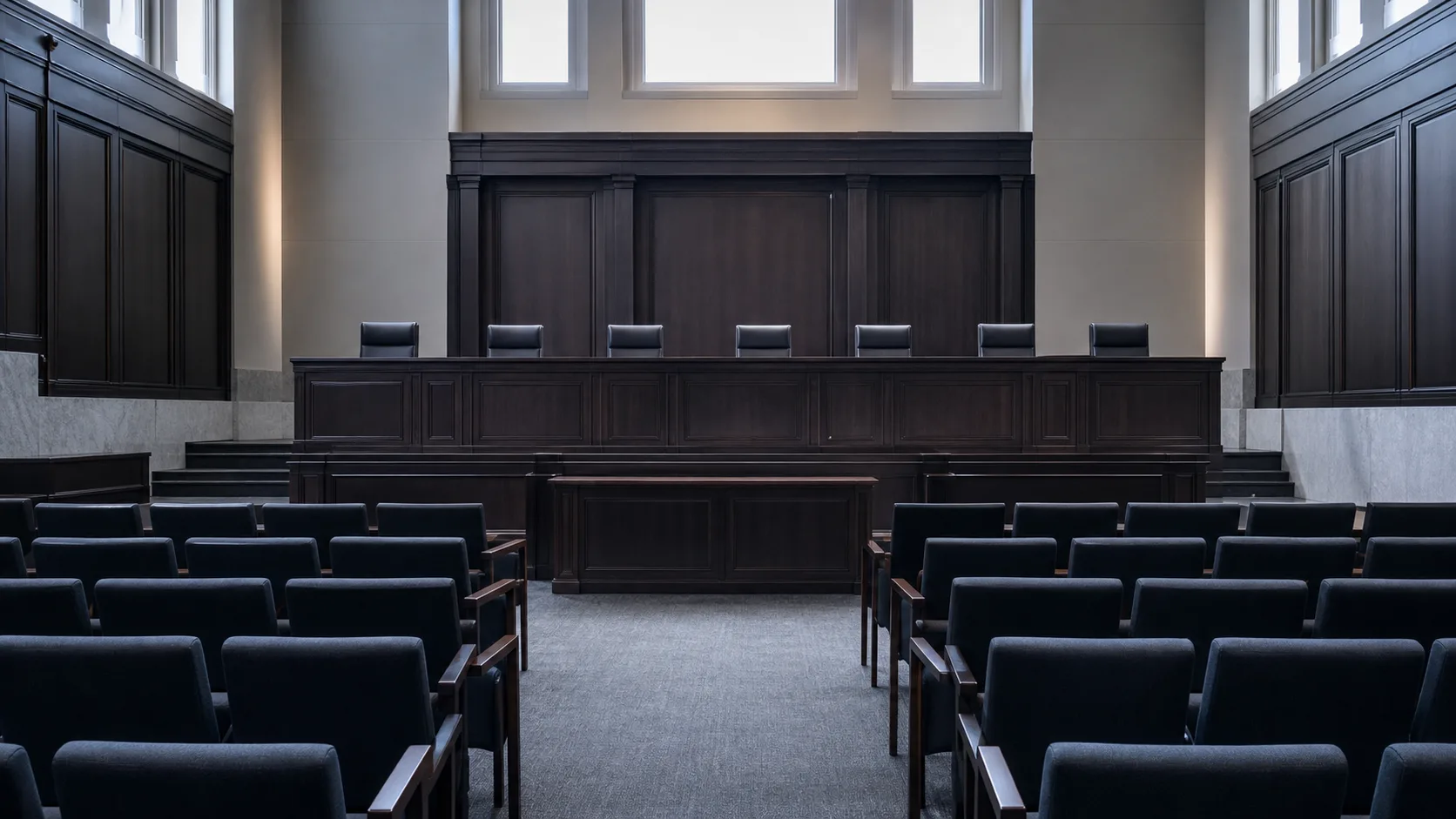 An empty formal hearing room with a raised panelled bench facing rows of chairs
