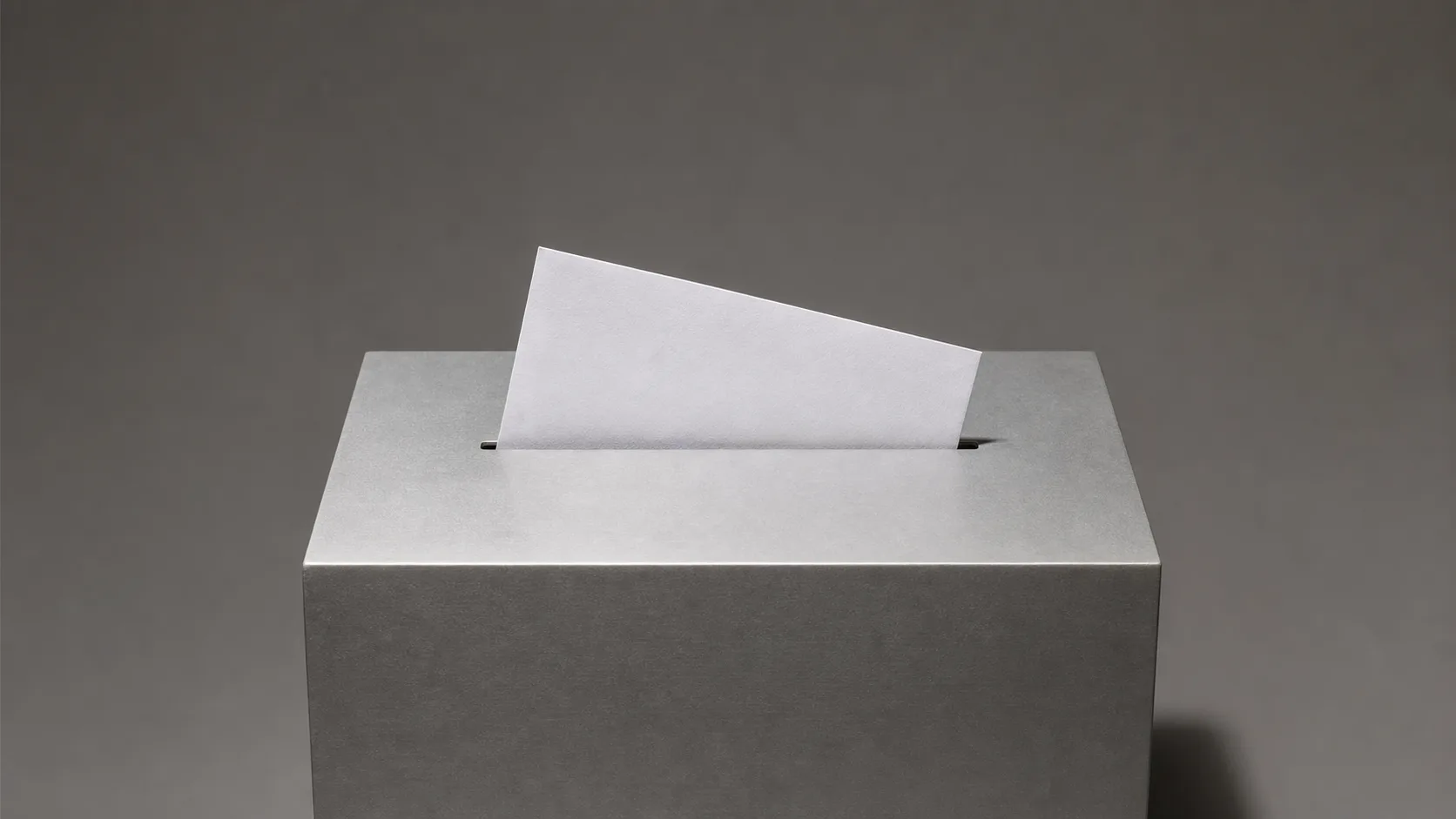 A plain unmarked envelope halfway into the slot of a featureless grey metal box