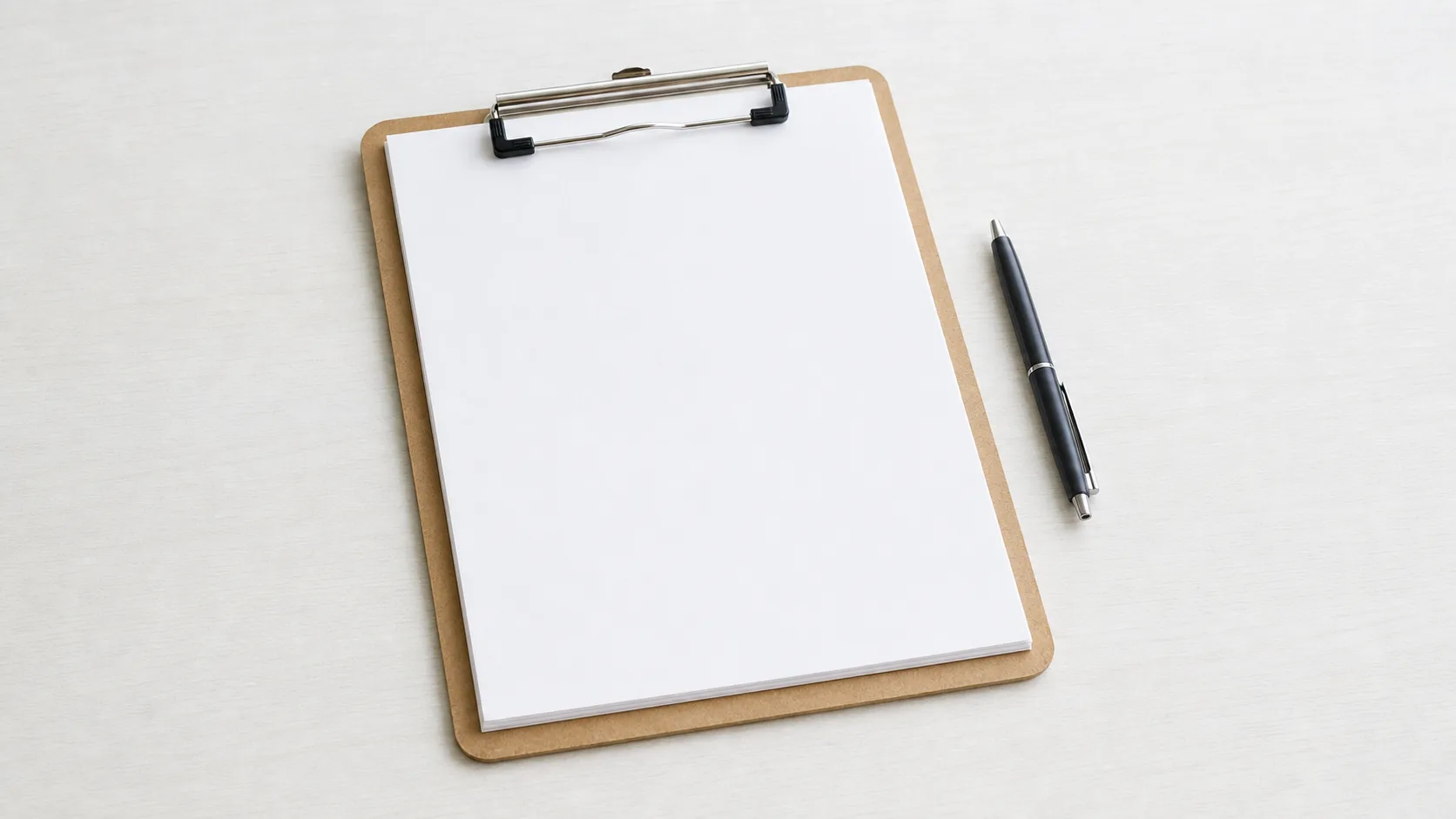A stack of identical blank forms on a clipboard beside a pen on a pale desk