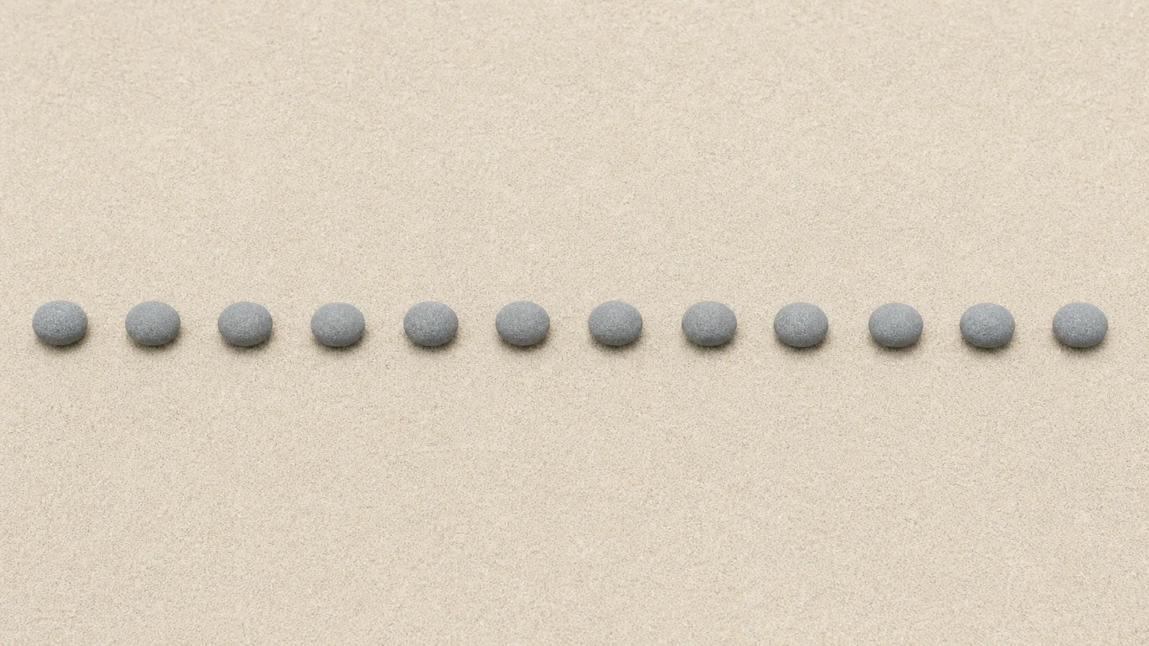 Twelve identical small stones arranged in an evenly spaced line across pale sand