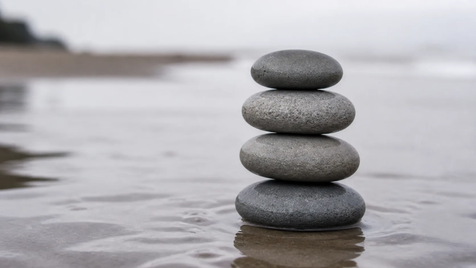 Four smooth grey stones balanced in a vertical stack on wet sand